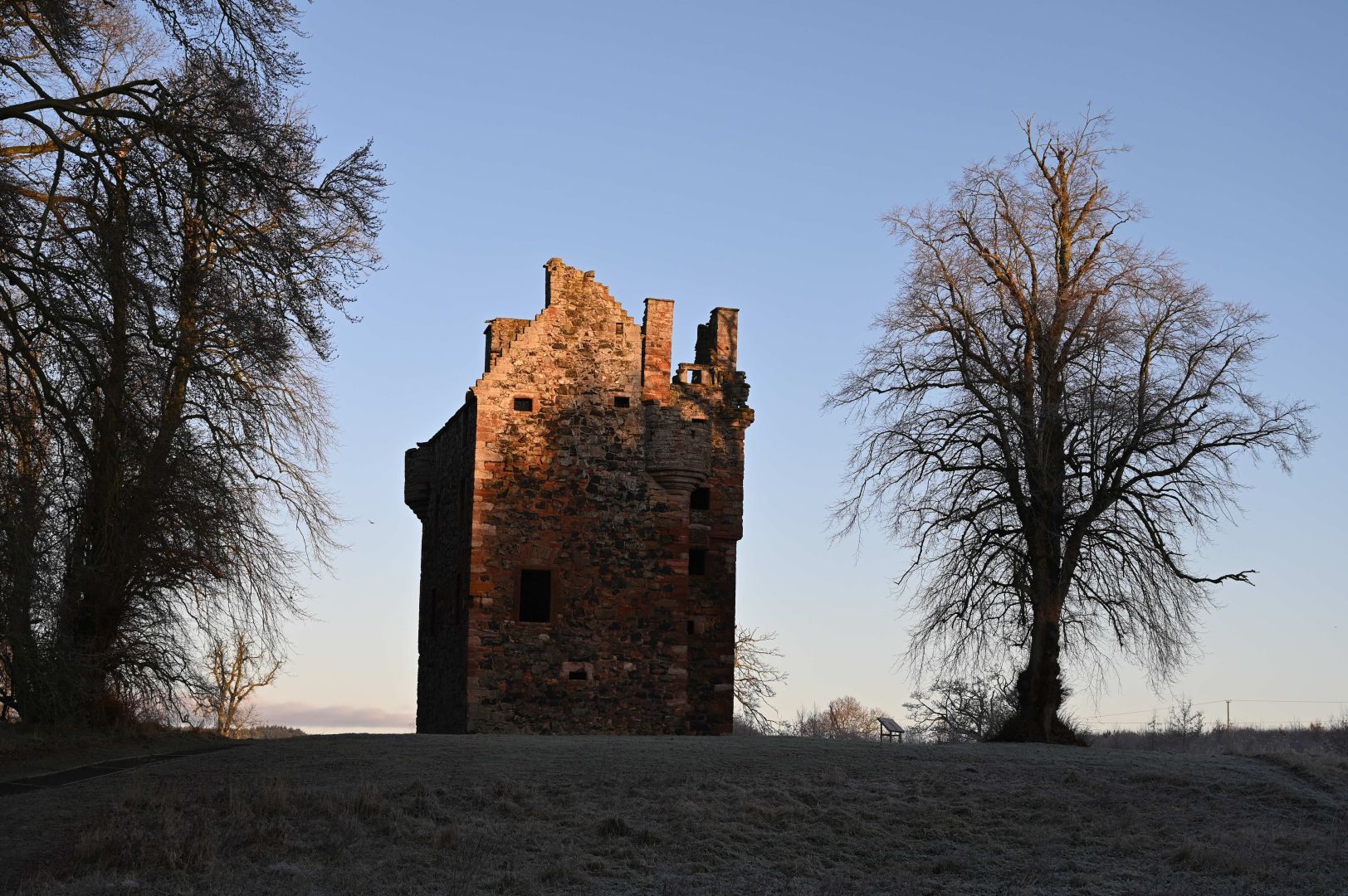 Greenknowe Tower, with sun starting to hit it as it rises with frost on the ground
